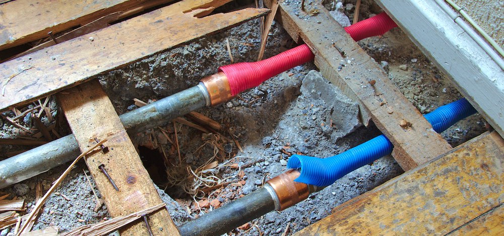 Cold and hot water pipes under a broken wood floor - unnoticed damage when the home is not occupied